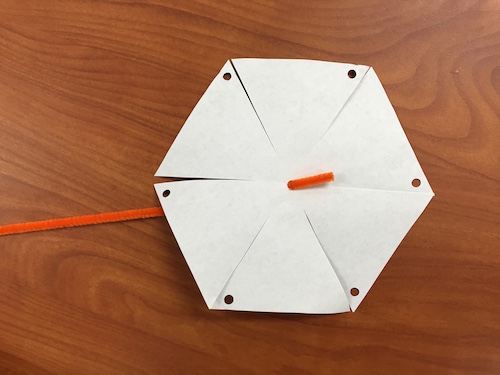 The hexagonal shape of the pinwheel galaxy printout turned on the opposite side so the white face is up, and the pipecleaner is threaded through the hole in the middle.