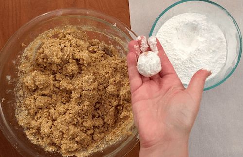 a person holds a finished moon cookie that is covered in powdered sugar.