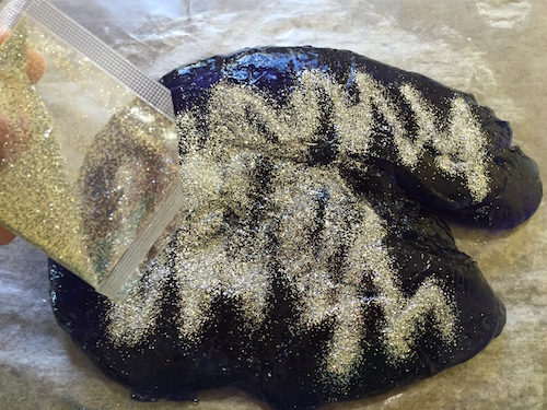 silver colored gliter is poured over the top of the hunk of slime